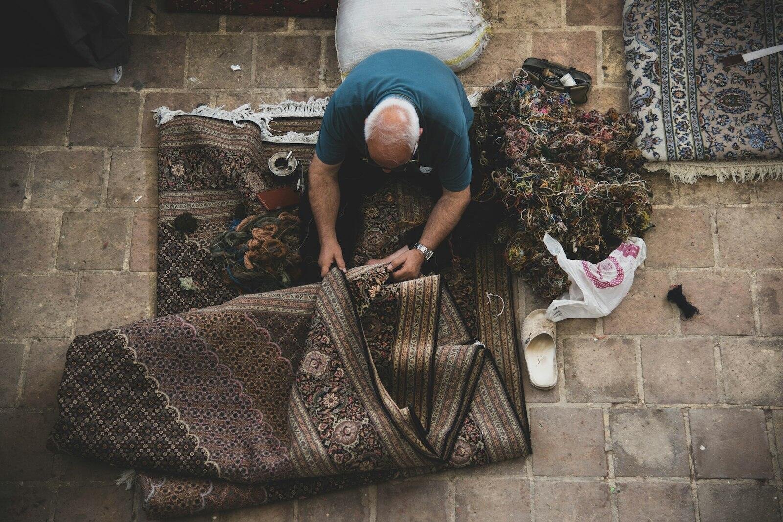 Desenli bir halıyı yerde katlayan usta